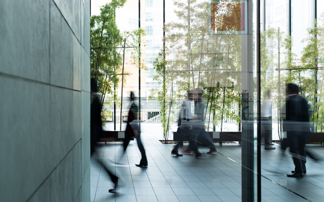 People walking through a modern glass building interior with trees visible outside and motion blur capturing movement